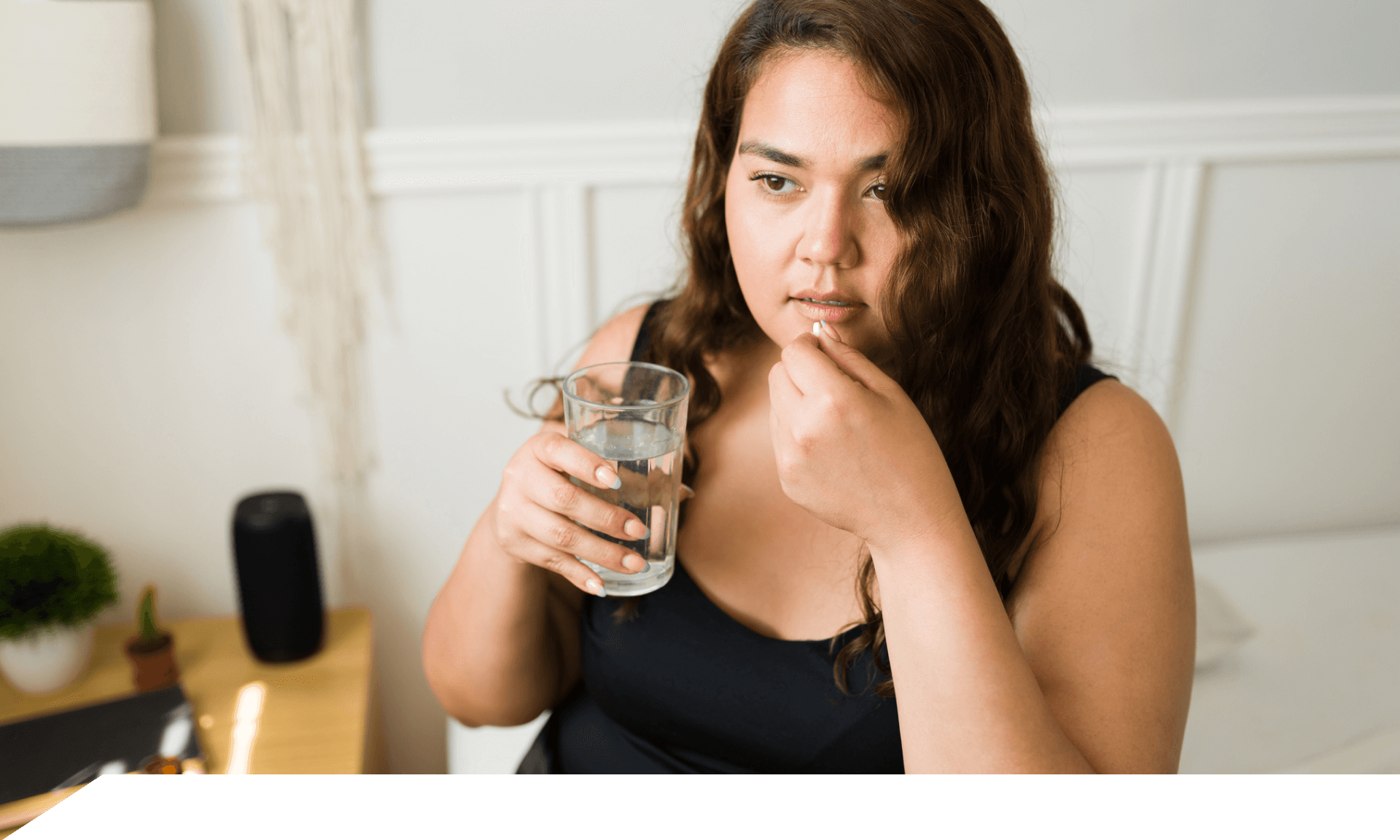 A woman holding a glass of water and a pill